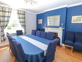 A dining room with a large table covered with a blue tablecloth and blue covered chairs by a window with blue and beige plaid curtains at Newton West Farm Newton near Newgale