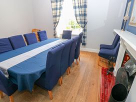 A dining room with a long table covered with a blue tablecloth and white runner surrounded by blue covered chairs next to a fireplace with red tiles and plaid curtains at Newton West Farm Newton near Newgale