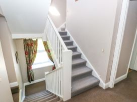 A staircase with grey carpet and white railing next to a window with floral curtains at Newton West Farm in Newton near Newgale