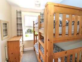 A small bedroom with wooden bunk beds a wooden chest of drawers a window with curtains and a wall mirror at Newton West Farm in Newton near Newgale