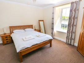 A bedroom with a wooden bed and bedside tables next to a window with curtains at Newton West Farm Newton near Newgale