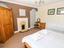 A bedroom with a wooden wardrobe a fireplace a dressing table with stool framed pictures on the wall and a bed with towels at Newton West Farm Newton near Newgale