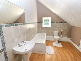 A bathroom with a sink, bathtub, toilet, small window, and wooden floor at Newton West Farm Newton near Newgale