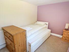 A bedroom with a white single bed with storage drawers underneath a towel on the bed a wooden chest of drawers a wooden bedside table with a lamp and walls painted in beige and purple at Newton West Farm Newton near Newgale