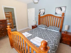 A bedroom with a wooden double bed with patterned bedding bedside tables with lamps a chest of drawers and bunk beds in an adjacent room at Newton West Farm in Newton near Newgale