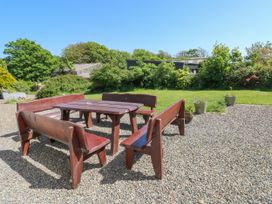 An outdoor seating area with wooden benches and a table on gravel with greenery in the background at Newton West Farm Newton near Newgale