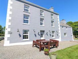 The exterior of a three-story gray building with white trim featuring windows and a door a wooden table with benches on a gravel area and flower pots nearby at Newton West Farm Newton near Newgale