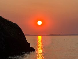 A sunset over water with a cliff on the left at Beach Cottage in Little Haven, Pembrokeshire