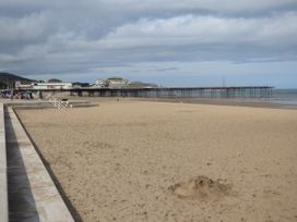 A sandy beach with a pier extending over the water and a concrete walkway along the edge at Coniston in Rhos Isaf