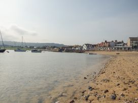 A beach with pebbles and boats on the water near houses and a harbor at Coniston in Rhos Isaf