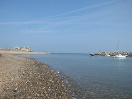A pebble beach with calm sea water and several boats near a rocky breakwater at Coniston in Rhos Isaf