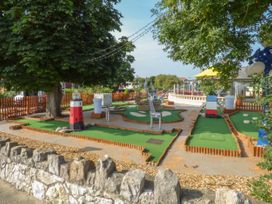 An outdoor mini golf course with green artificial turf and themed obstacles surrounded by trees and a stone wall at Coniston in Rhos Isaf