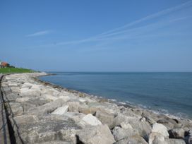 A rocky shoreline with calm sea and clear sky with walkway and grassy area at Coniston in Rhos Isaf