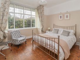 A bedroom with a metal bed frame a chair by a large window and butterfly pictures on the wall at Coniston in Rhos Isaf