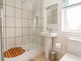 A bathroom with a shower enclosure a wooden shower mat a pedestal sink a mirror a toilet a waste bin and a window at Coniston in Rhos Isaf