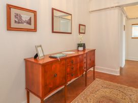 A wooden sideboard with drawers and cabinets below a wall mirror and framed pictures in a hallway with a rug on the floor at Coniston in Rhos Isaf