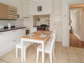 A kitchen with a wooden table and white chairs next to a cooking stove at Coniston in Rhos Isaf