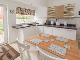 A kitchen with a wooden table and white chairs next to cabinets and a window with a floral blind at Coniston in Rhos Isaf
