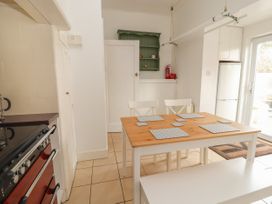 A kitchen with a wooden dining table set with placemats two white chairs a bench a refrigerator a stove a white door and a green wall shelf at Coniston in Rhos Isaf