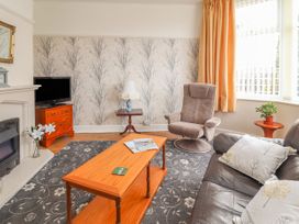A living room with a brown sofa and armchair a wooden coffee table a television on a cabinet and a window with orange curtains at Coniston in Rhos Isaf