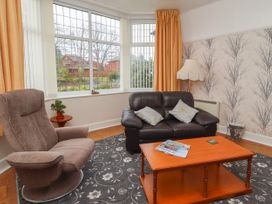 A living room with a brown armchair a black leather sofa a wooden coffee table and large windows at Coniston in Rhos Isaf