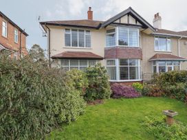 A front garden with green grass and various bushes in front of a semi detached house with bay windows at Coniston in Rhos Isaf