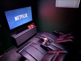 A home theater with recliners and a television displaying Netflix at The Hideout in Lanreath