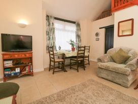 A living room with a television on a wooden cabinet a small dining table with four chairs a single armchair and a wall clock at The Old Coach House in Penmaenmawr