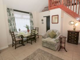 A living area with a table and chairs near a window an armchair a small side table a chest of drawers and stairs at The Old Coach House in Penmaenmawr