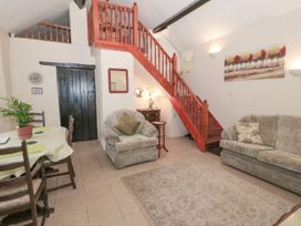 A living room with a dining table chairs sofas a rug a wooden staircase a wooden door and wall decorations at The Old Coach House in Penmaenmawr