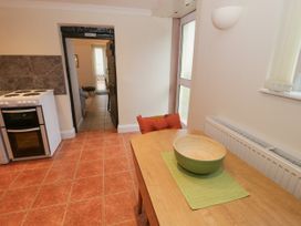 A kitchen with a wooden table and bowl near a white stove and a doorway leading to a living room at The Old Coach House in Penmaenmawr