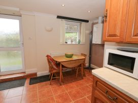 A kitchen with a wooden table and chairs a microwave on the counter and a window at The Old Coach House in Penmaenmawr