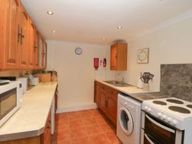 A kitchen with wooden cabinets a microwave washing machine and stove at The Old Coach House in Penmaenmawr