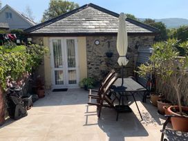 A patio area with a table and chairs an umbrella potted plants and a stone building with white double doors at The Old Coach House in Penmaenmawr
