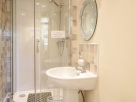 A bathroom with a glass shower enclosure a white pedestal sink a round mirror and a soap dispenser at The Old Coach House in Penmaenmawr