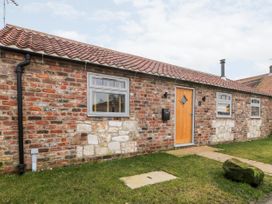 The exterior view of a single-story brick house with a tiled roof wooden door and three grey framed windows with grass in front at 1 Church Barns in Pocklington
