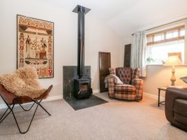 A living room with a wood stove a leather chair a tartan armchair and a lamp on a side table at 1 Church Barns in Pocklington