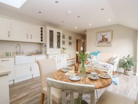 A kitchen and dining area with a round wooden table set with plates and cups a sofa with cushions a plant and cabinets at 1 Church Barns in Pocklington