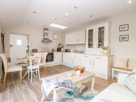 A kitchen and dining area with a table and chairs a coffee table with a newspaper and a bowl of fruit and a bench with cushions at 1 Church Barns in Pocklington