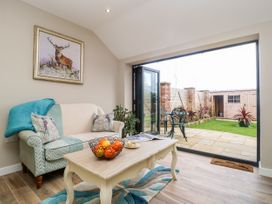 A living room with a sofa, coffee table with fruit bowl, and open glass doors leading to a small garden with patio and shed at 1 Church Barns in Pocklington