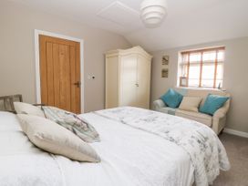A bedroom with a bed with pillows a wooden door a cream wardrobe a sofa with cushions and a window at 1 Church Barns in Pocklington