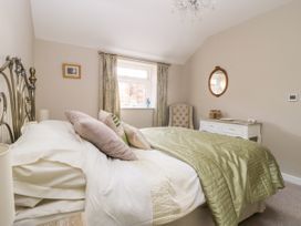 A bedroom with a bed with green bedding pillows beside a window with curtains and a white dresser with a mirror at 1 Church Barns in Pocklington