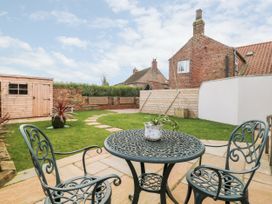 A backyard with a metal table and two chairs on a stone patio a wooden shed and brick houses at 1 Church Barns in Pocklington