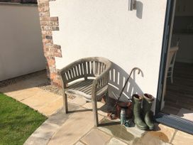 An outdoor area with a wooden chair boots an umbrella a thermos and a bag near a white wall and glass door at 1 Church Barns in Pocklington