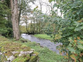 A tree beside a river with a stone wall and grass at Smithy Cottage at Bowland Bridge, Bowness