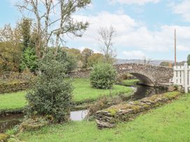 A bridge over a stream with trees and grass at Smithy Cottage at Bowland Bridge Bowness