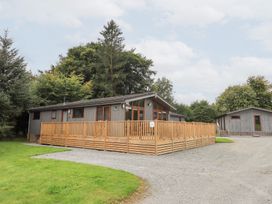 A wooden lodge with a deck and trees at The Loghey in Hawkshead