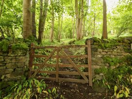 A wooden gate next to a stone wall in a forest at Durham Bridge Barn in Crosthwaite