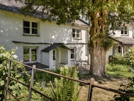 The exterior of a white building with windows a small porch a large tree and a table with two chairs on a patio at High Lindeth in Bowness