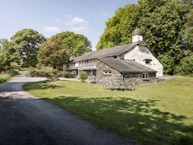 A country house with a stone extension and outdoor metal table and chairs on a lawn at High Lindeth in Bowness